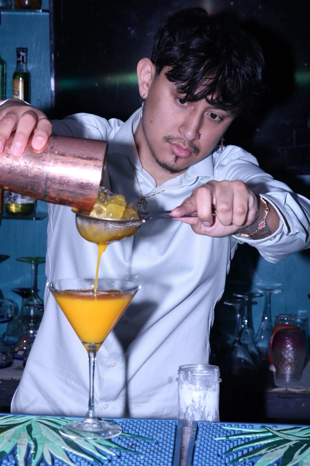A bartender pouring an orange cocktail through a strainer at Hacienda Santa Teresa