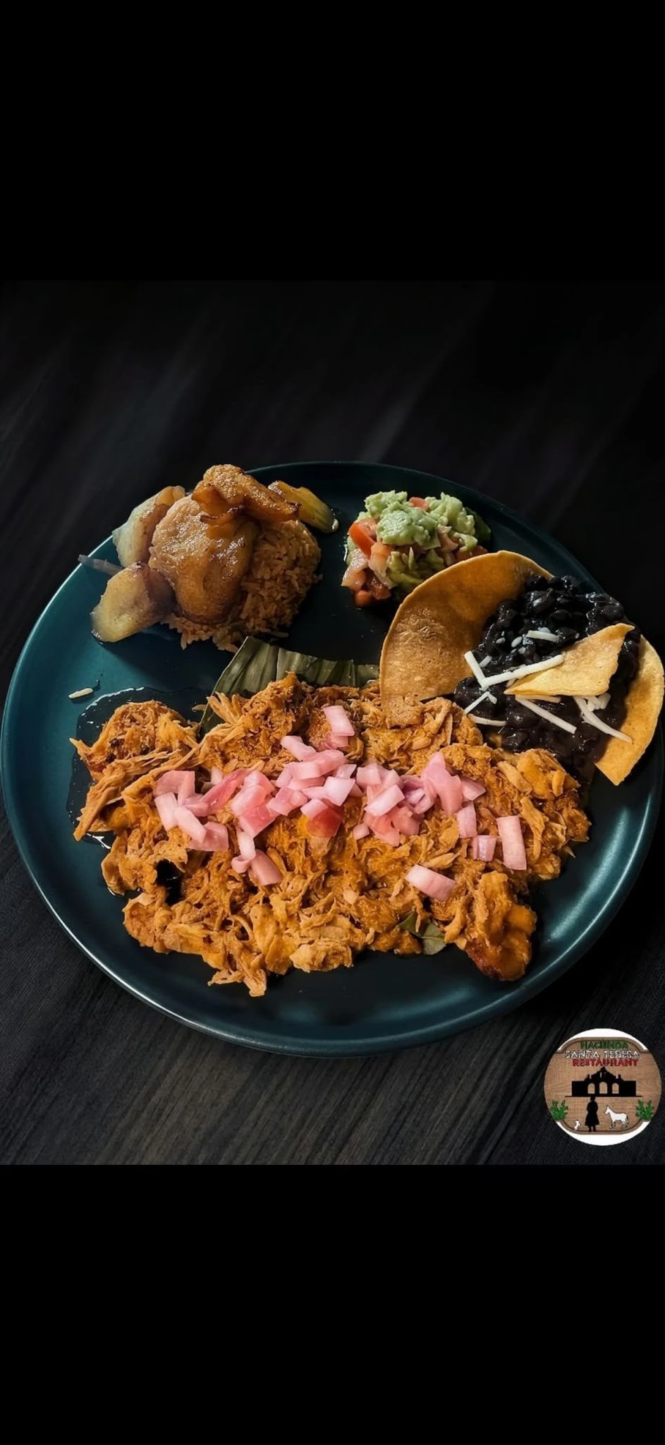Cochinita pibil topped with pickled onions, served with plantains, rice, beans, and guacamole