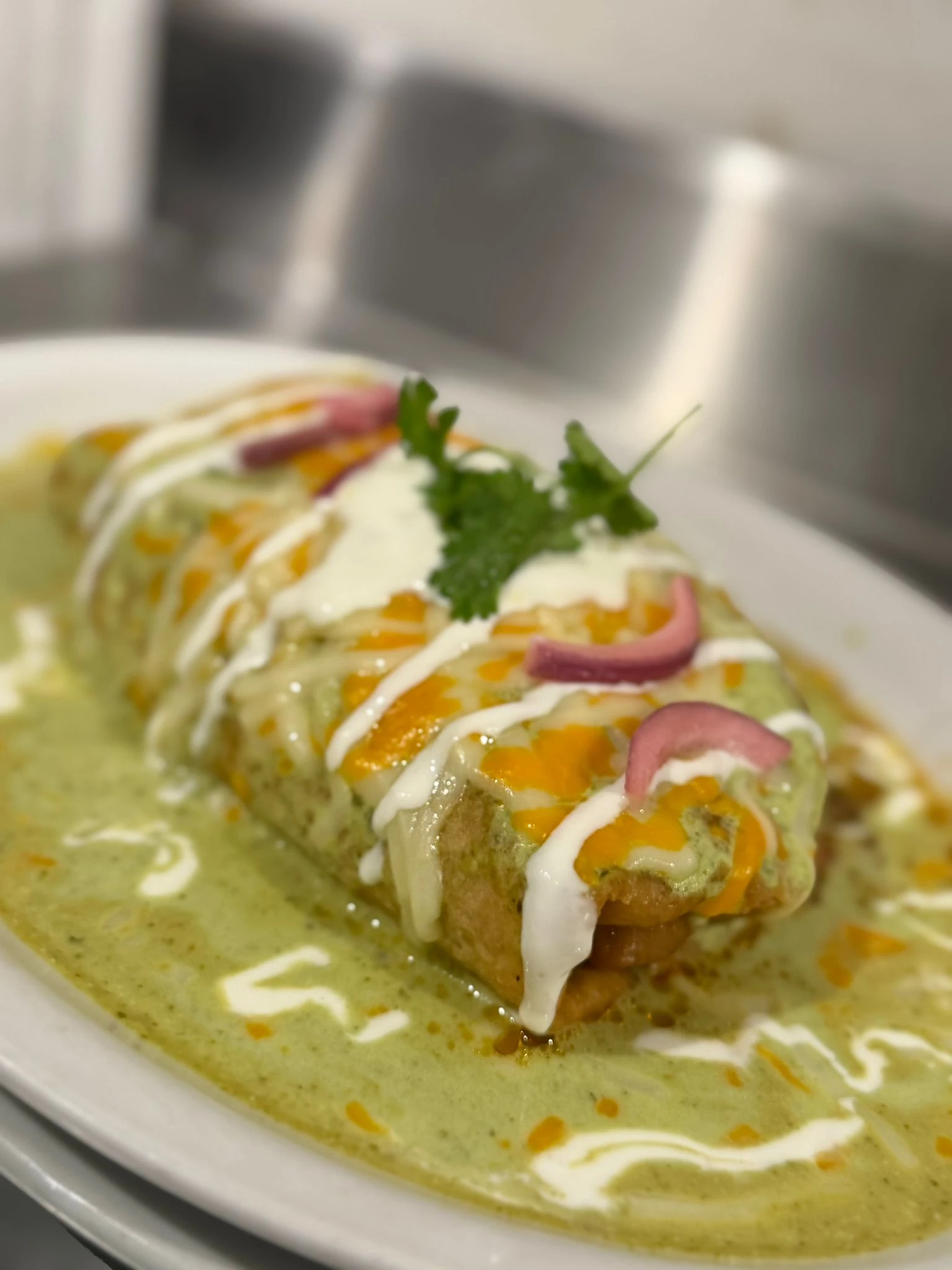 A Mexican dish covered in creamy green sauce, melted cheese, pickled onions, and herbs at Hacienda Santa Teresa