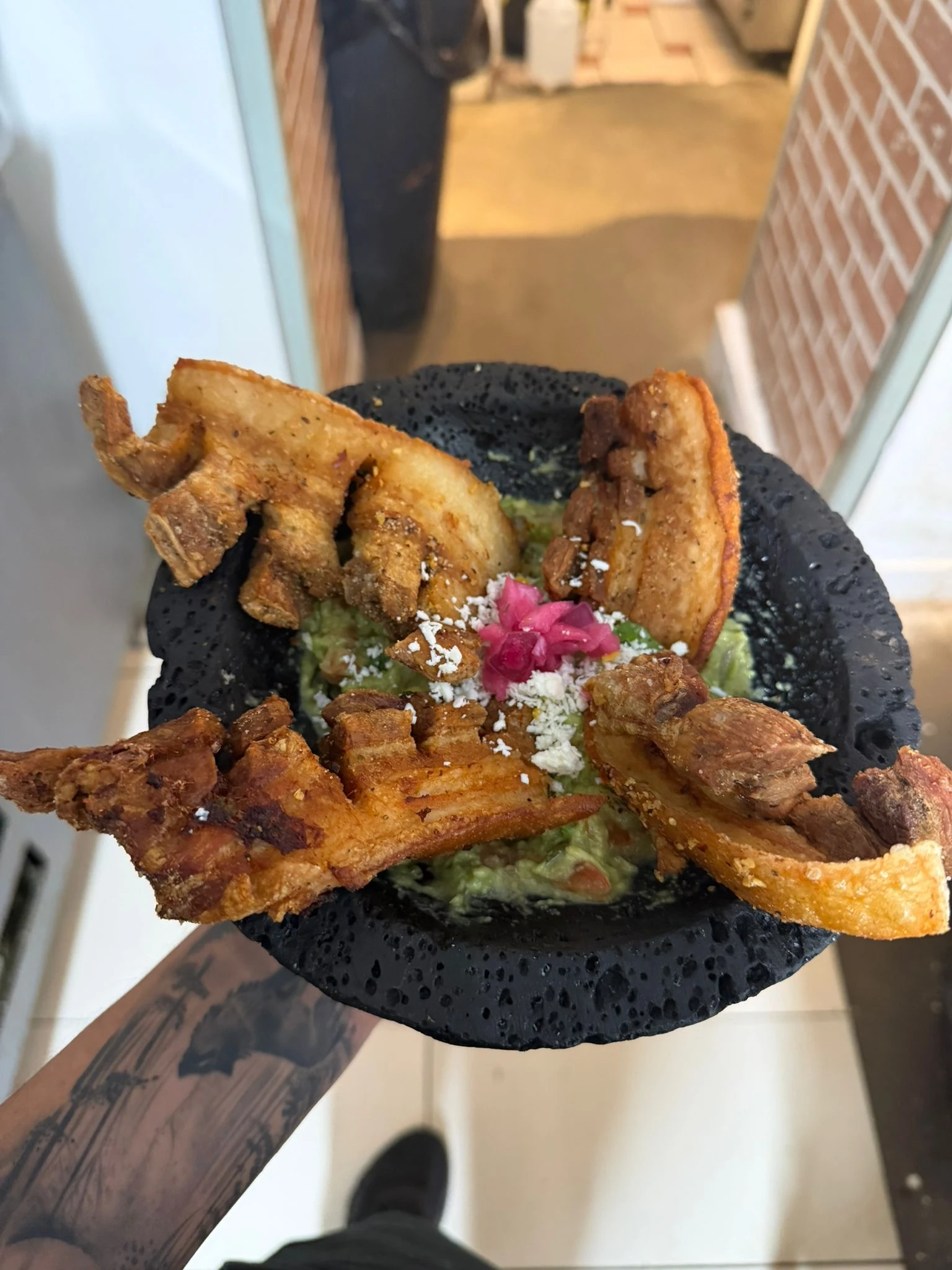 Crispy pork pieces around guacamole in a black stone bowl at Hacienda Santa Teresa