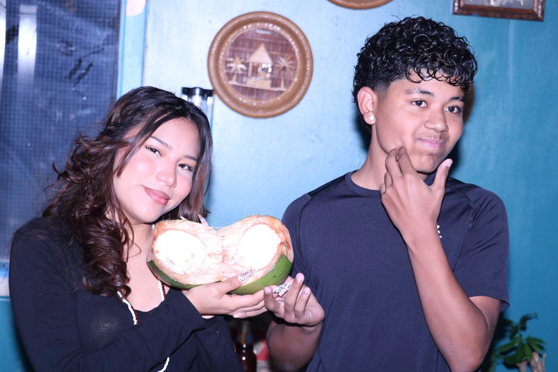 Two guests holding a freshly opened coconut against Hacienda Santa Teresa’s blue wall