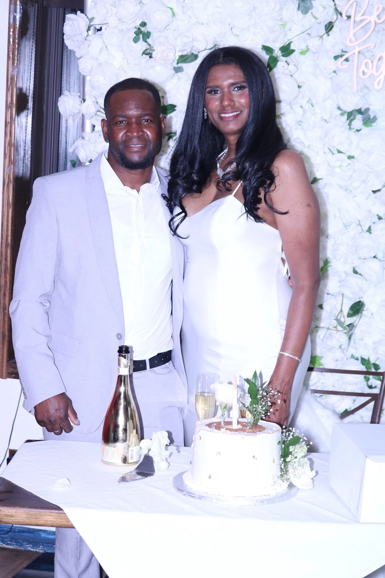 A wedding couple smiling beside their cake and flowers at Hacienda Santa Teresa