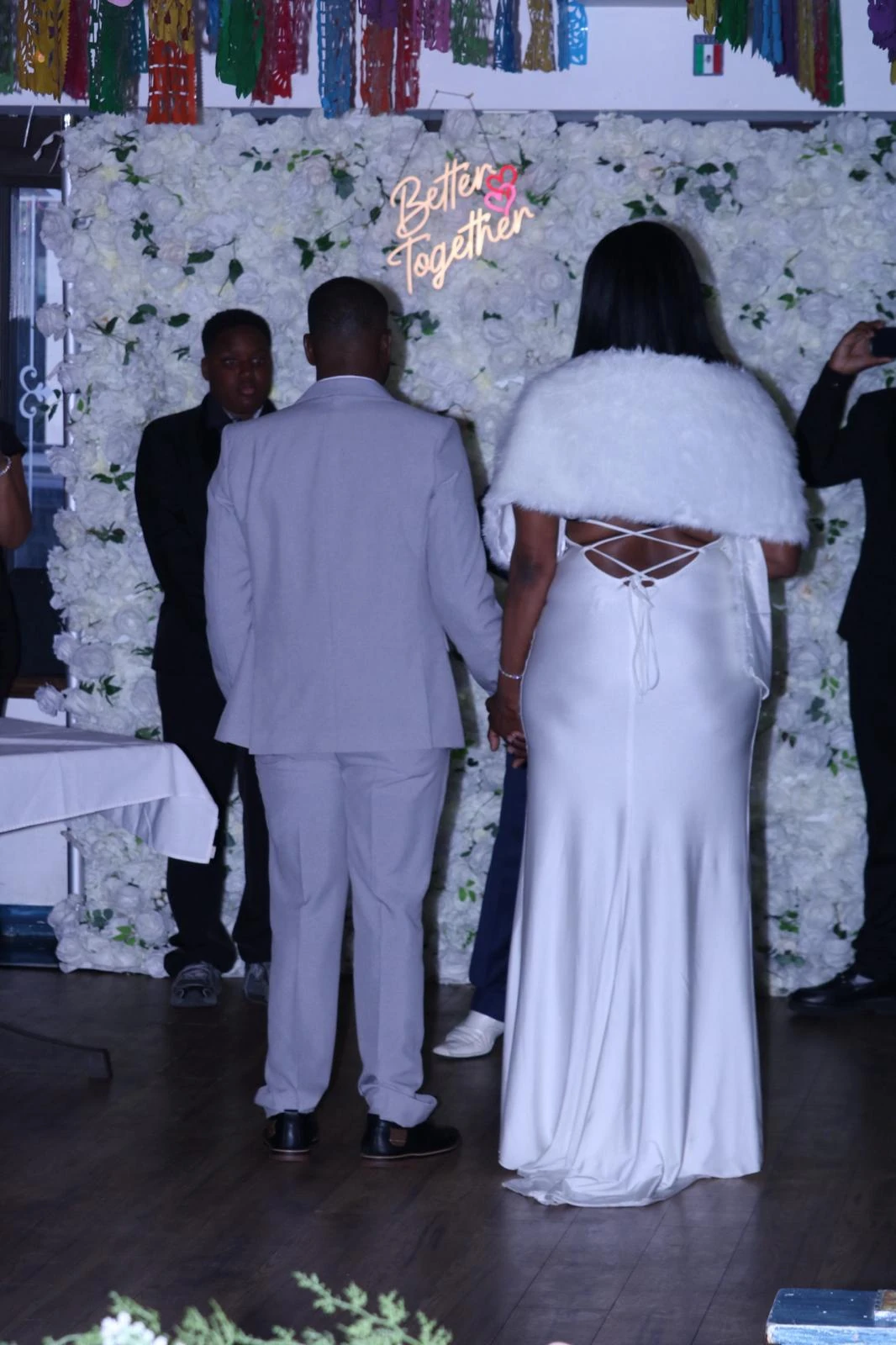 A wedding couple holding hands in front of a white floral backdrop inside Hacienda Santa Teresa