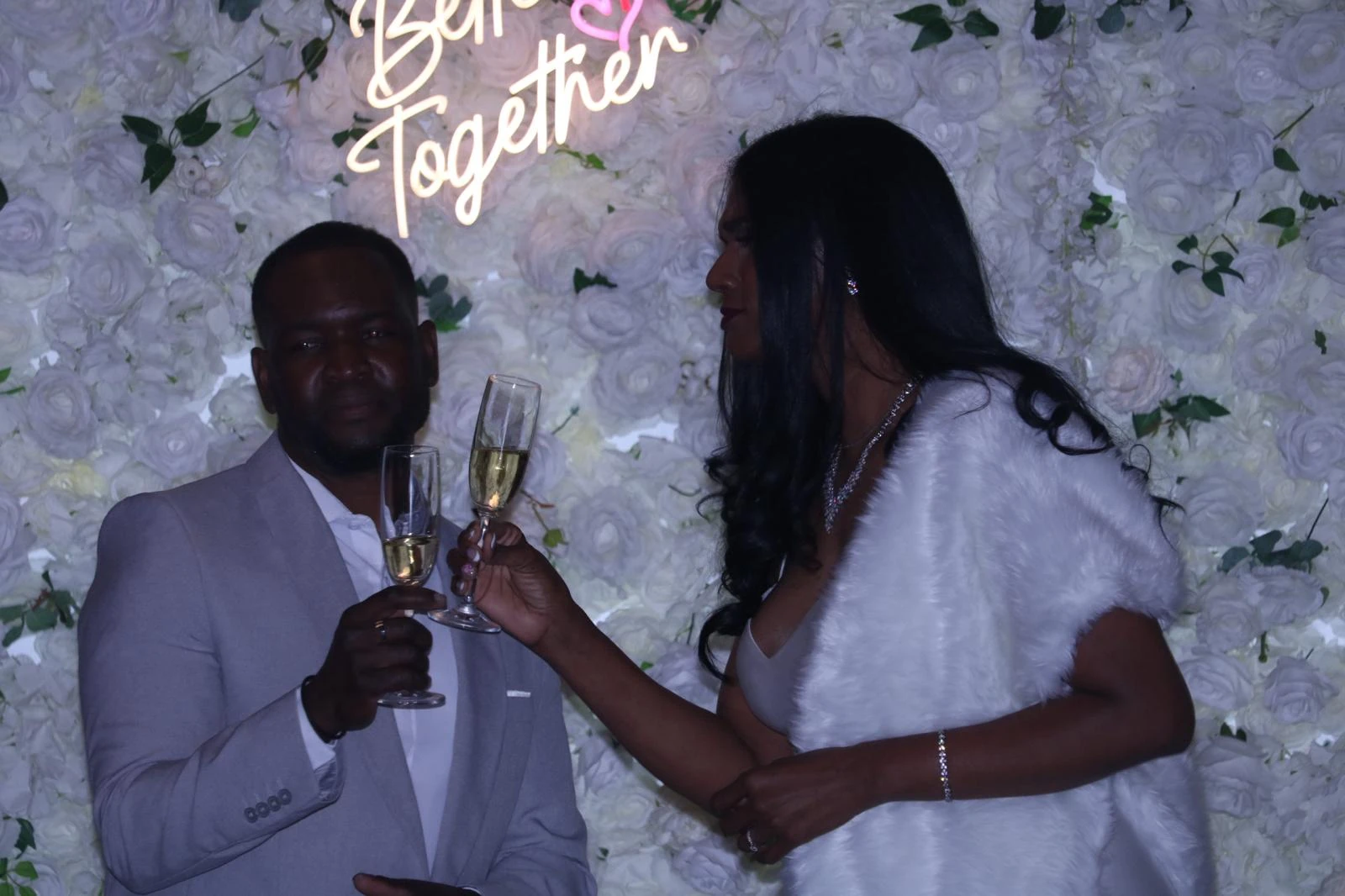 A wedding couple raising glasses in front of a white floral wall at Hacienda Santa Teresa